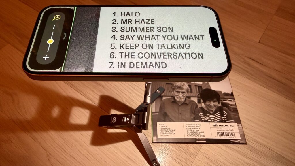 Das Bild zeigt ein iPhone 15, welches auf dem Stativ montiert ist. Das Stativ steht auf der CD "The Muscle Shoals Sessions" von Texas. Vergrößert wird die Tracklist.